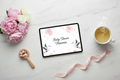 Digital baby shower notebook displayed on a tablet, flat lay on white marble with pink flowers and baby props