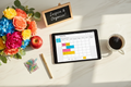 Digital teacher planner on a tablet, flat lay on white marble with colorful flowers, red apple, gold pen, paper clips and coffee